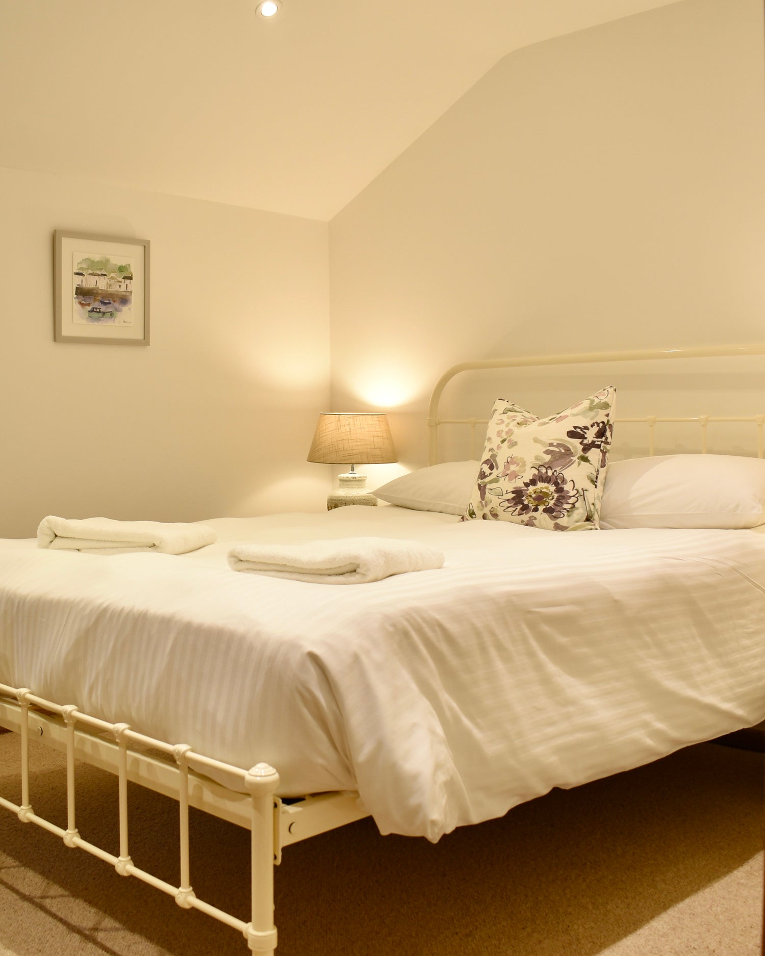 Neatly made bed in a bedroom with a lamp and framed picture on the wall.