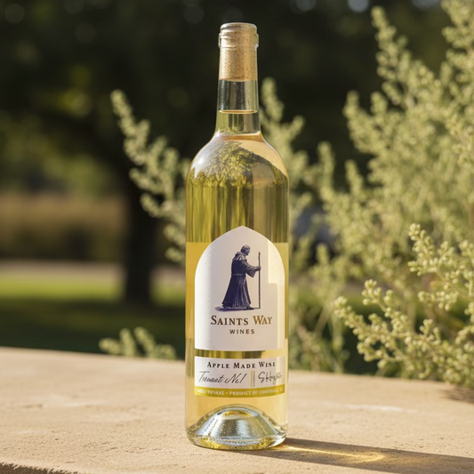 A bottle of Saint's Way Wines Apple Wine, showing the clear glass bottle filled with pale yellow wine and a white label with a blue saint illustration.