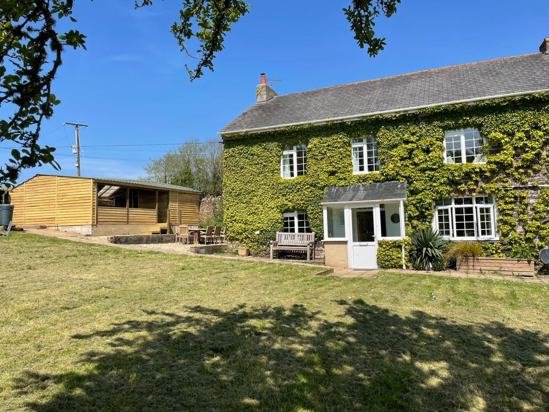 Image of the front of the farmhouse at Trenant - a Green ivy-covered house with a garden on a sunny day.