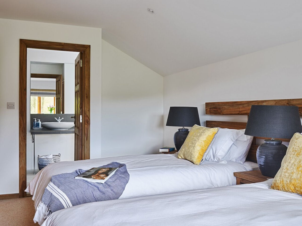 Bedroom with two beds, lamps, and a bathroom visible through a doorway.