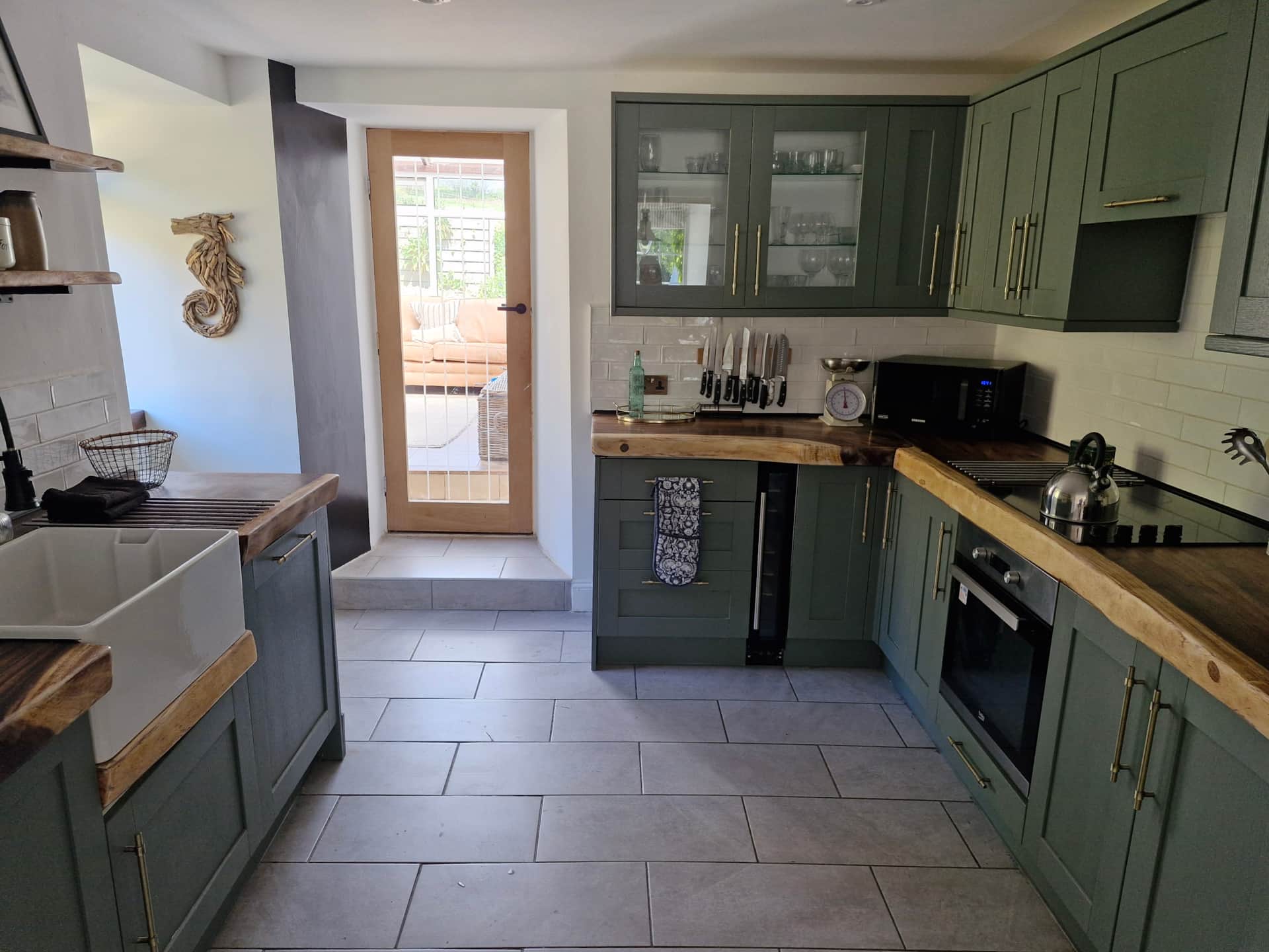 Modern kitchen with green cabinets, wooden countertops, and tiled floor.